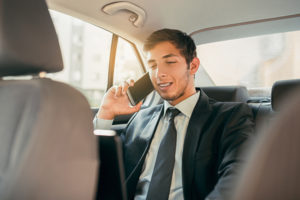 Businessman working while sitting in a car. Man beeing driven to work in his limo. Suit and tie businessman in the back seat making a call while the limo driver is driving.