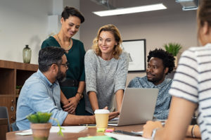 Multiethnic business people talking and smiling during meeting in office. Mature middle eastern man explaining proposal. Happy businessman showing project and marketing strategy on laptop to colleague