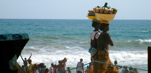 Women walking with full bowls on their heads near a beach - Explore Cote D’Ivoire