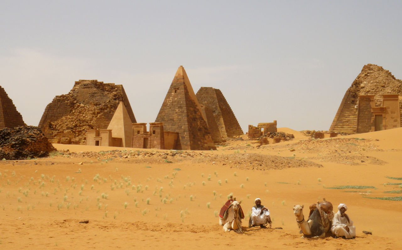Men sitting with camels in front of ancient pyramids