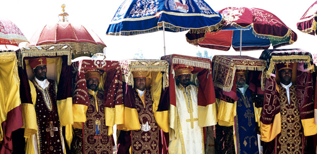 Men in highly embellished clothing under the shade of their hats and umbrellas
