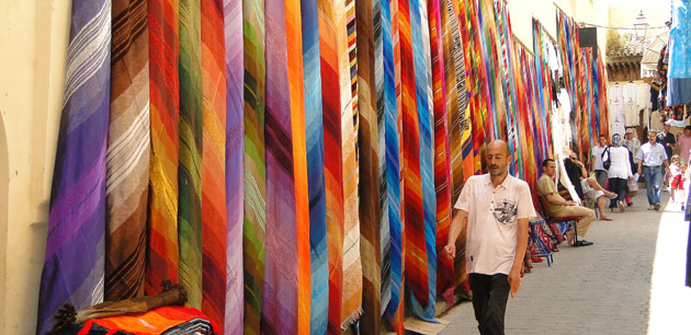 A wall covered with colorful cloths with men walking by