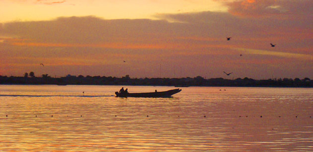 Men in a boat being silhouetted against a sunset - Pink Lake