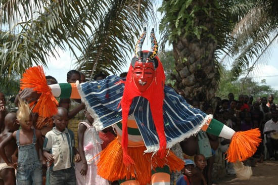 A person in wearing a red mask and colorful clothing dancing - Cultural & Historical Côte d'Ivoire